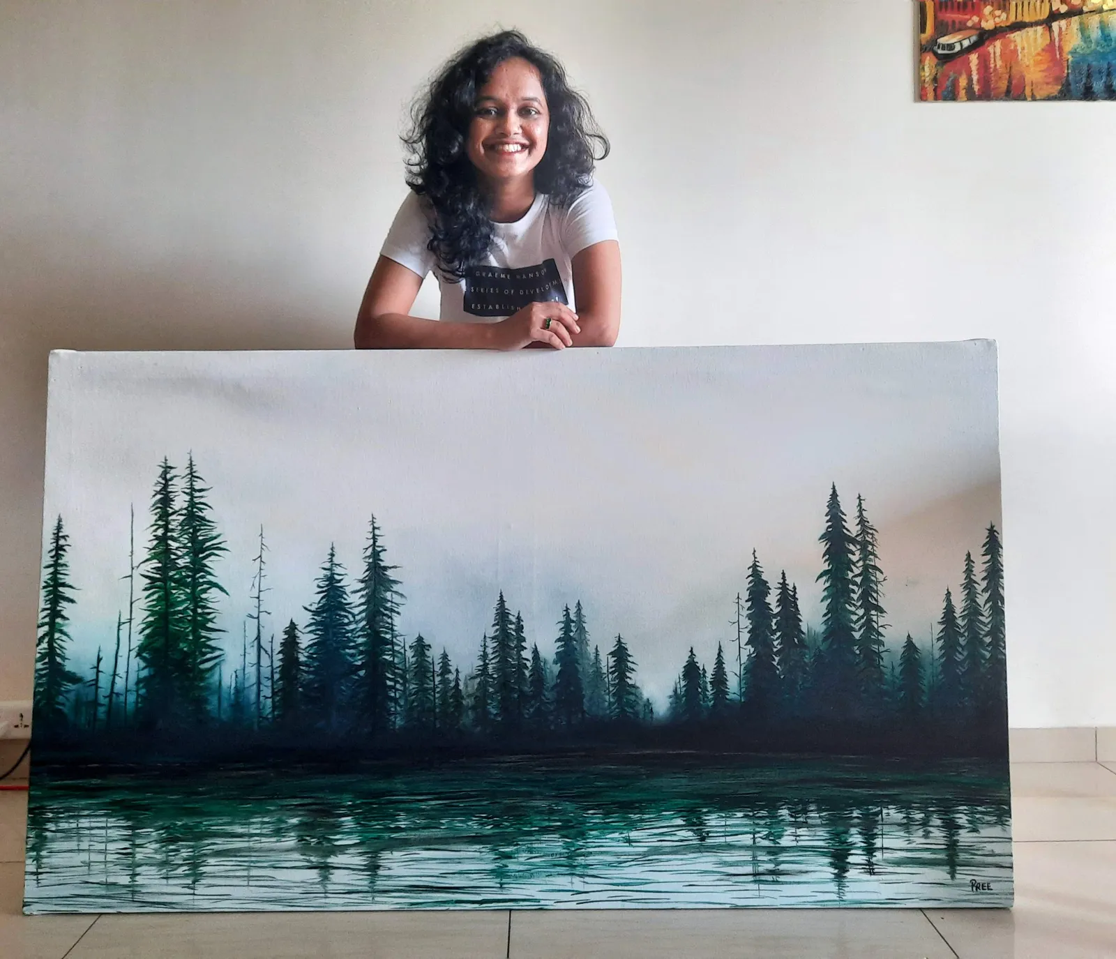 Priyasha standing outdoors holding her framed Misty Forest painting